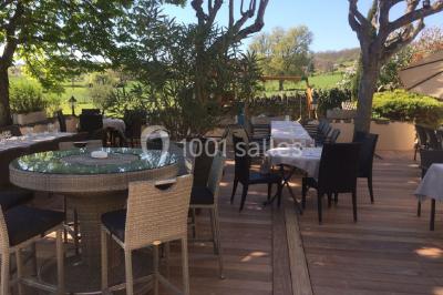 Menu posé sur une table dressée en extérieur, entourée de verres, fleurs et paysage verdoyant en arrière-plan.