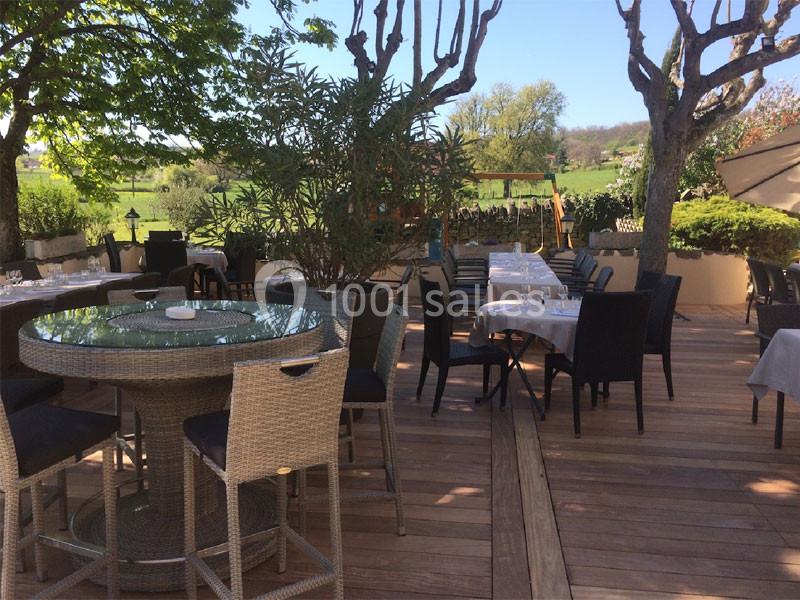 Terrasse en bois aménagée avec tables et chaises, entourée de verdure et d'arbres, sous un ciel dégagé.