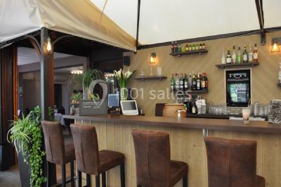 Menu posé sur une table dressée en extérieur, entourée de verres, fleurs et paysage verdoyant en arrière-plan.