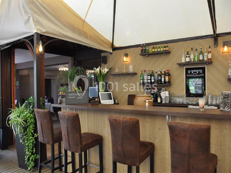 Bar en bois avec tabourets en cuir, étagères de bouteilles, plantes décoratives et éclairage chaleureux.