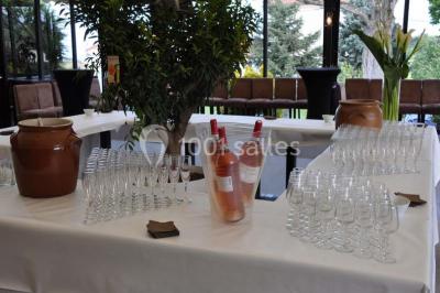 Menu posé sur une table dressée en extérieur, entourée de verres, fleurs et paysage verdoyant en arrière-plan.