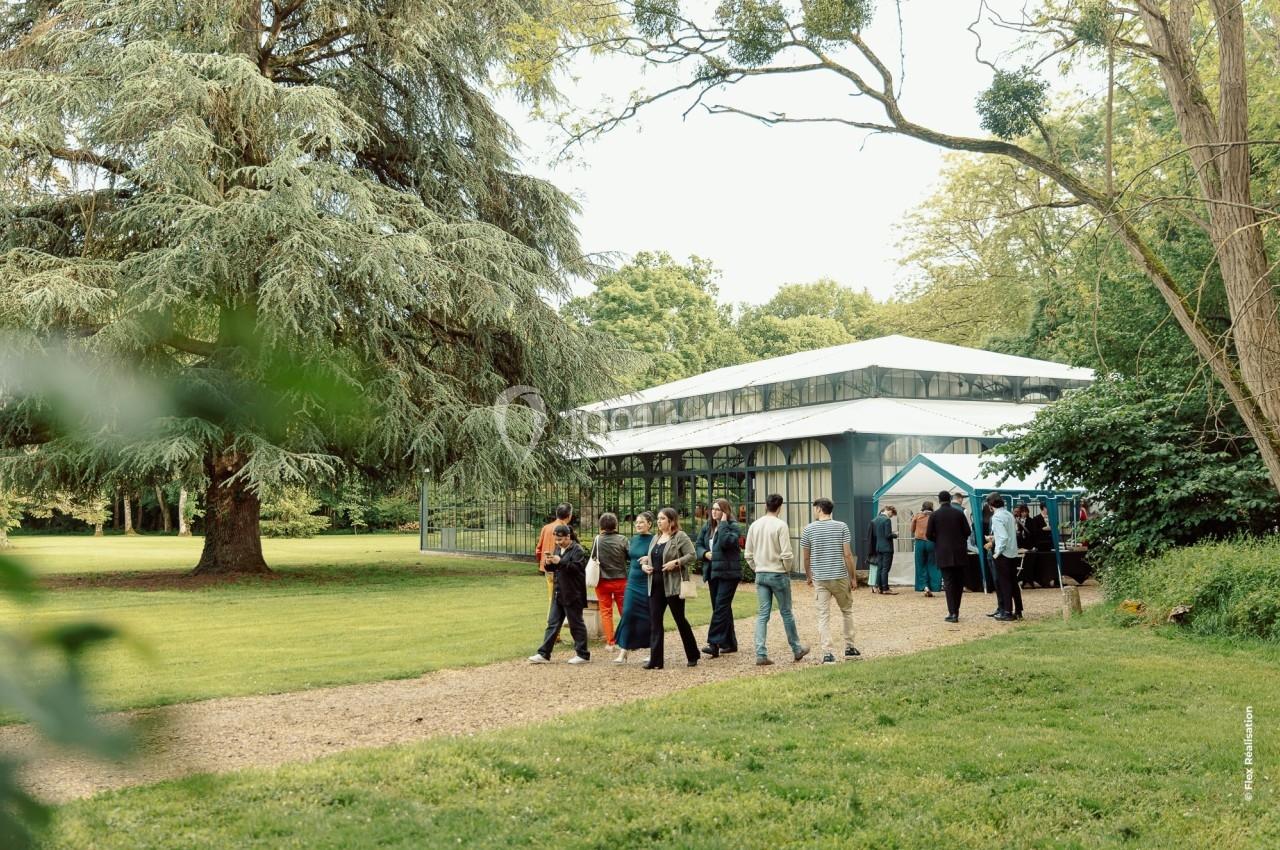 Un groupe de personnes se tient près d'un bâtiment vitré entouré de verdure dans un parc.