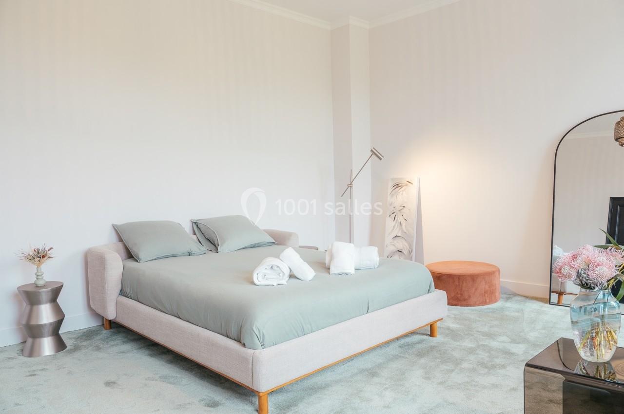 Chambre lumineuse avec un lit double, linge de maison plié, miroir, lampe sur pied et décoration florale.