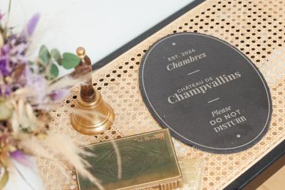 Plaque ’Château de Champvallins’ sur une table en rotin avec une cloche dorée et une boîte décorative.