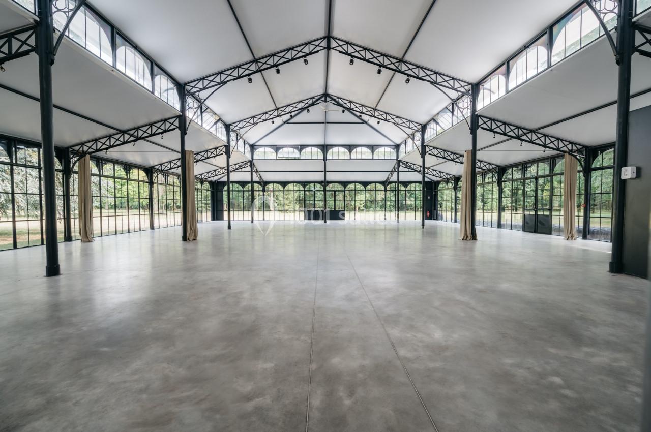 Intérieur d'une grande salle lumineuse avec structure métallique, murs vitrés et sol en béton poli.