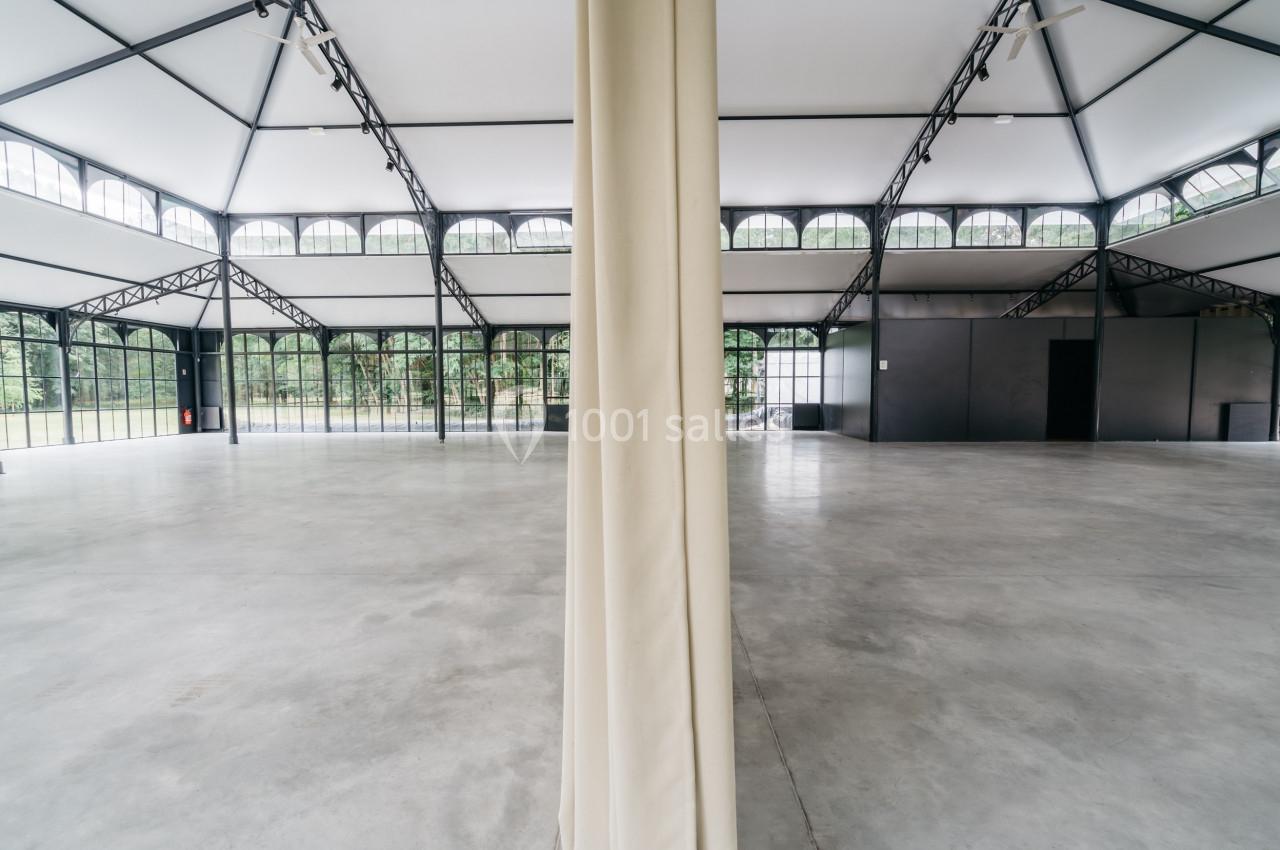 Intérieur d'une grande salle lumineuse avec structure métallique, sol en béton et rideau central divisant l'espace.
