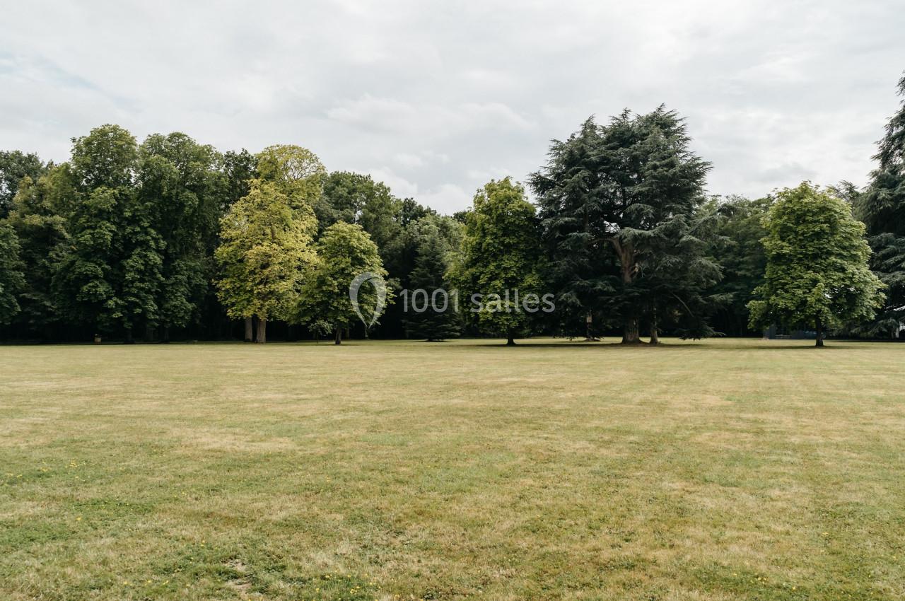 Pelouse verdoyante entourée d'arbres dans un parc sous un ciel légèrement nuageux.