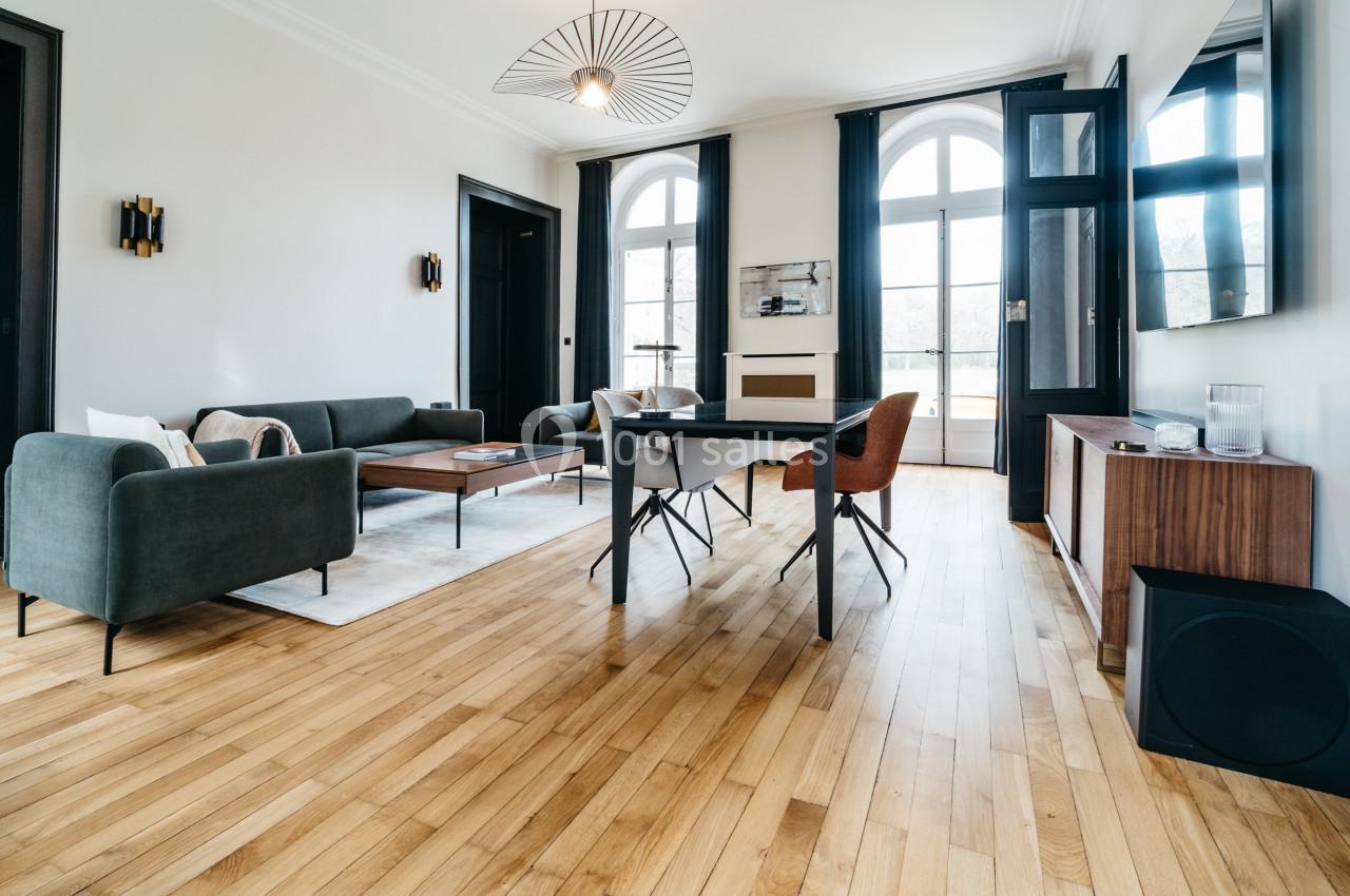 Salon lumineux avec parquet en bois, mobilier moderne, grandes fenêtres cintrées et décoration épurée.