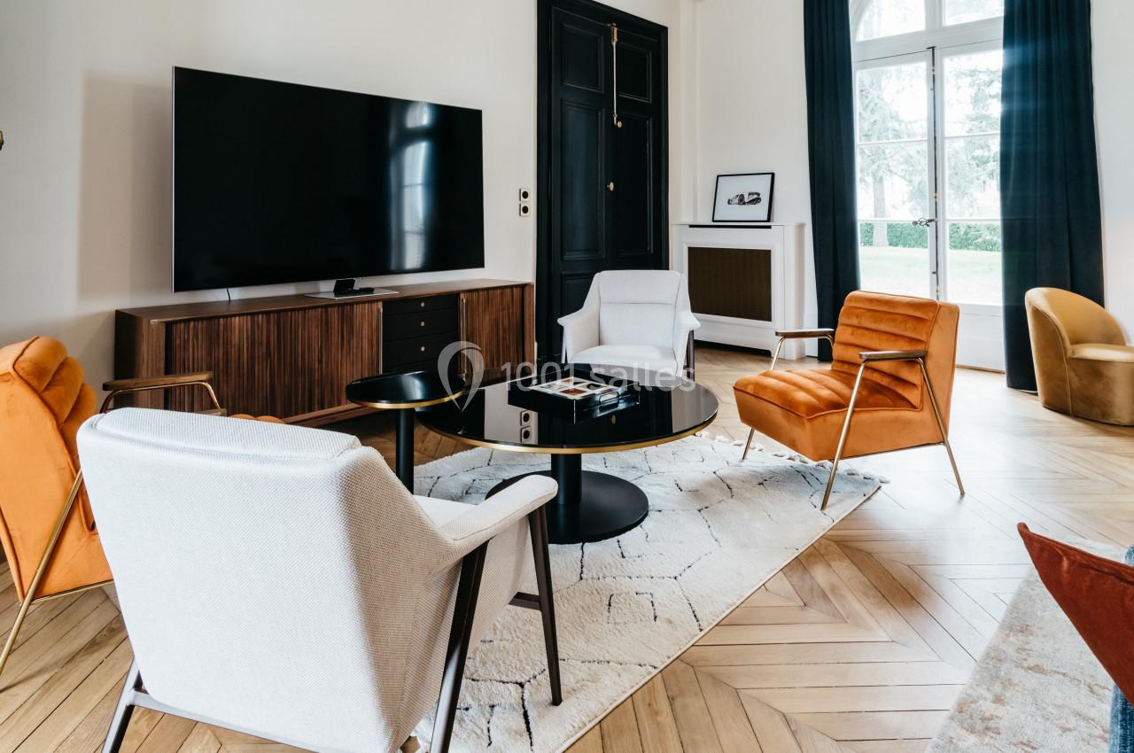 Salon moderne avec fauteuils colorés, table basse noire, tapis clair, meuble TV en bois et grande télévision murale.