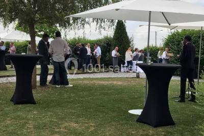 Groupe de personnes discutant dans un jardin sous des parasols, avec des tables hautes recouvertes de nappes noires.