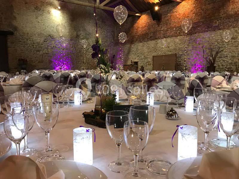 Salle de réception décorée avec des tables dressées, des verres, des bougies lumineuses et des ballons suspendus.