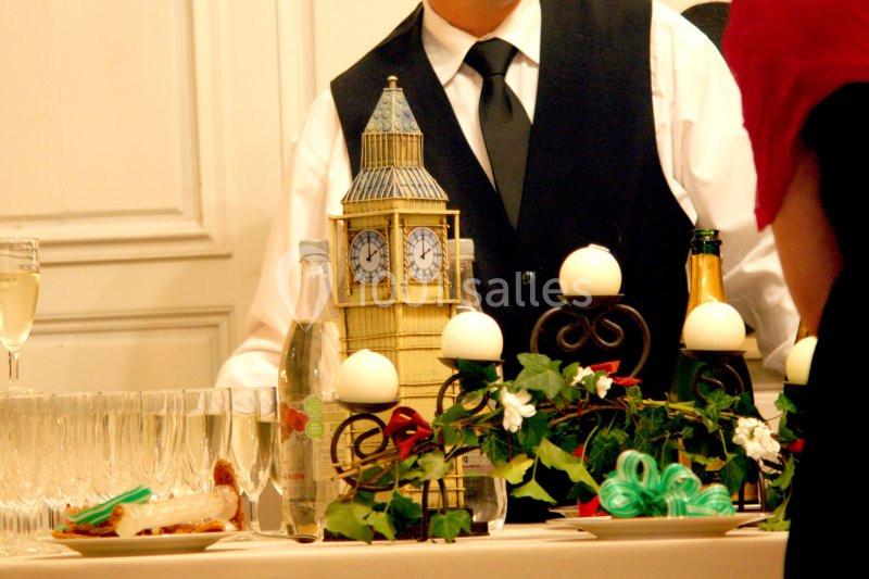 Un serveur en gilet noir derrière une table décorée avec des bougies, des plantes et une réplique de Big Ben.