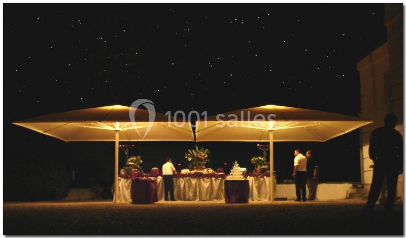 Deux grands parasols éclairés abritent une table décorée pour un événement nocturne en plein air.