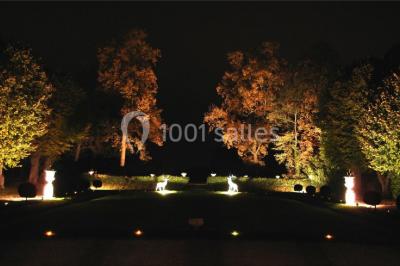 Un parc de nuit avec des arbres sombres, une structure lumineuse orange et des chemins faiblement éclairés.