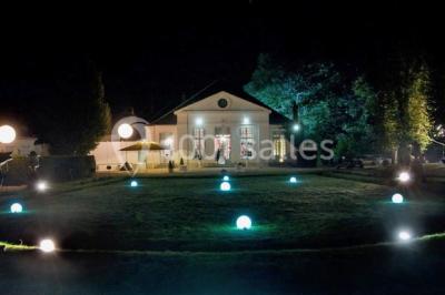 Un parc de nuit avec des arbres sombres, une structure lumineuse orange et des chemins faiblement éclairés.