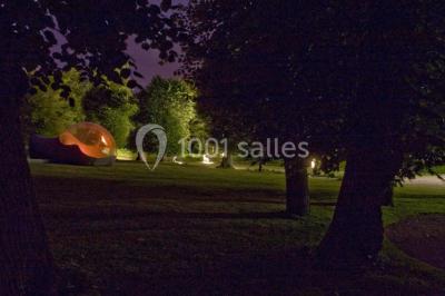 Un parc de nuit avec des arbres sombres, une structure lumineuse orange et des chemins faiblement éclairés.