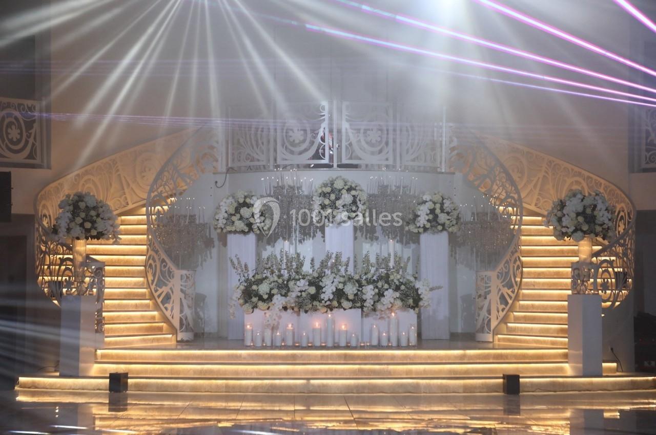Décor de cérémonie avec escalier illuminé, fleurs blanches, chandeliers et éclairage tamisé.