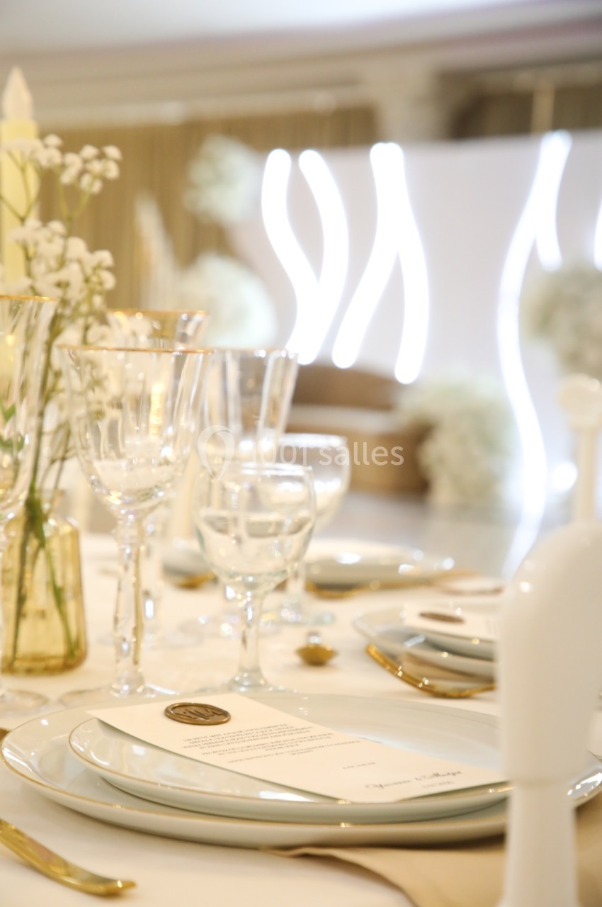 Table élégamment dressée avec vaisselle raffinée, verres en cristal et décoration florale blanche dans un cadre lumineux.