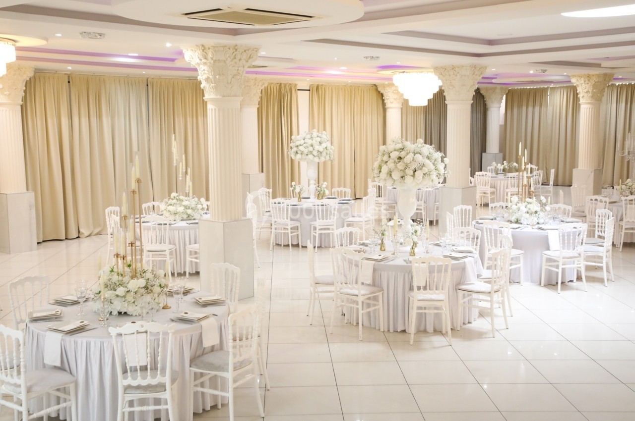 Salle de réception élégante avec tables rondes décorées de nappes blanches, chaises assorties et arrangements floraux.
