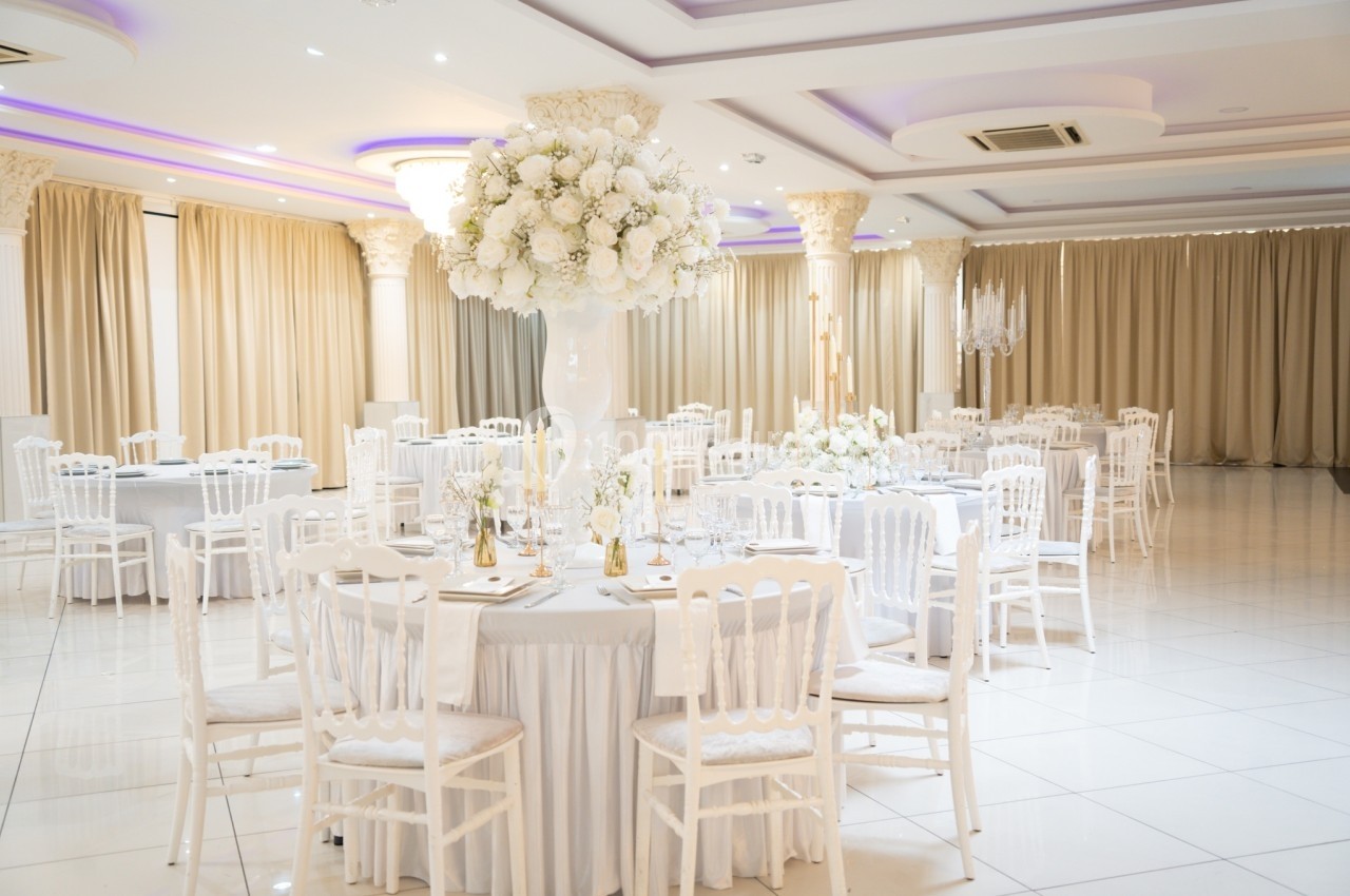 Salle de réception élégante avec tables rondes décorées de nappes blanches, chaises assorties et centres de table fleuris.
