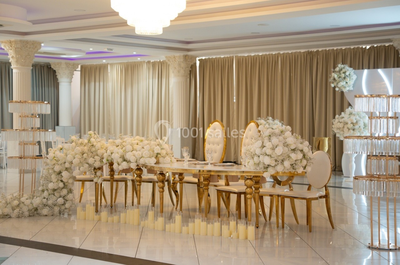 Salle de réception décorée avec des chaises dorées, une table ornée de fleurs blanches et des rideaux beiges en arrière-plan.