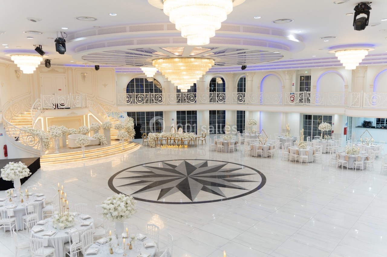 Salle de réception élégante avec tables décorées, chandeliers et grand lustre central sous un plafond orné.