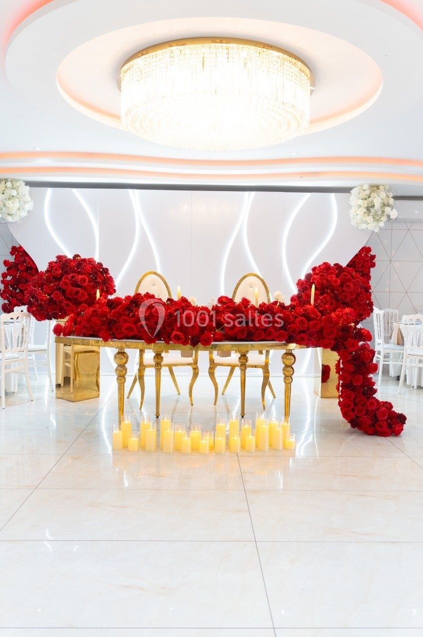 Table décorée de roses rouges, entourée de bougies allumées, sous un lustre lumineux dans une salle élégante.