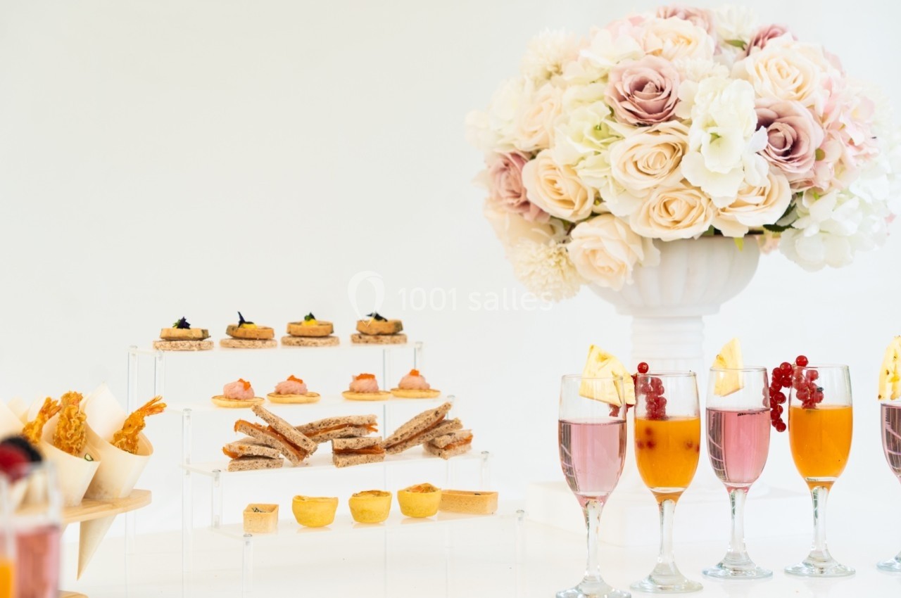 Buffet élégant avec amuse-bouches, verrines colorées et un bouquet de fleurs pastel en arrière-plan.