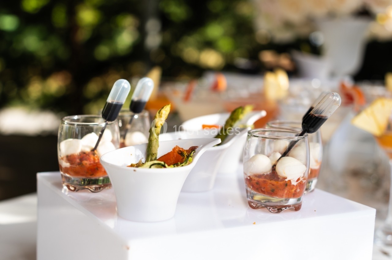 Assortiment de verrines et amuse-bouches avec légumes, mozzarella et pipettes de sauce, présenté sur une table.
