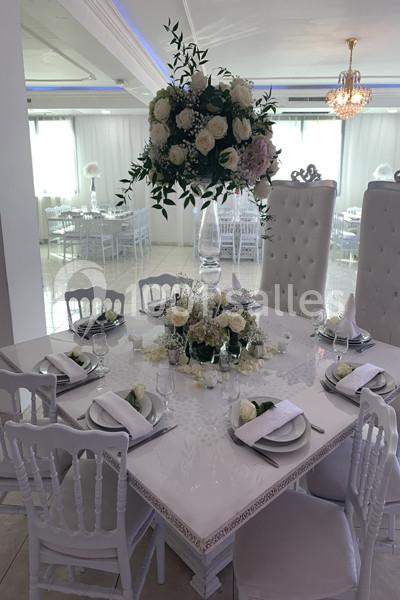 Table élégamment dressée avec des assiettes blanches, serviettes pliées et un grand centre de table floral.