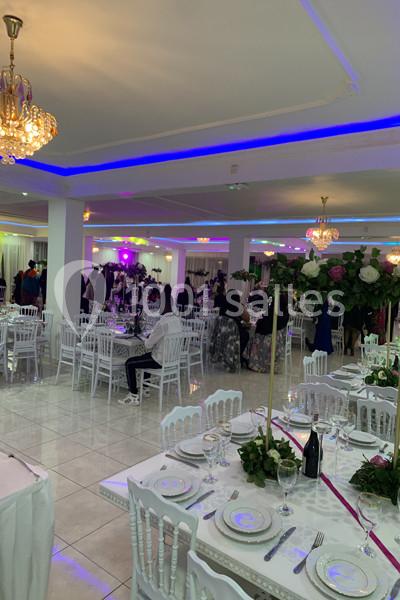 Salle de réception décorée avec des tables dressées, des chaises blanches et des éclairages colorés au plafond.