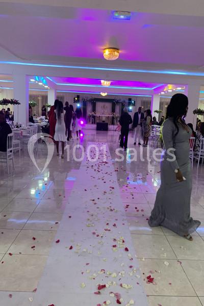 Allée décorée de pétales de rose dans une salle de réception éclairée, avec des invités en arrière-plan.