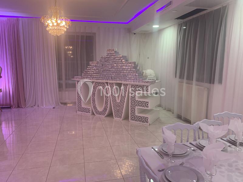 Décoration de salle avec des lettres géantes formant ’LOVE’, éclairage violet et table dressée au premier plan.