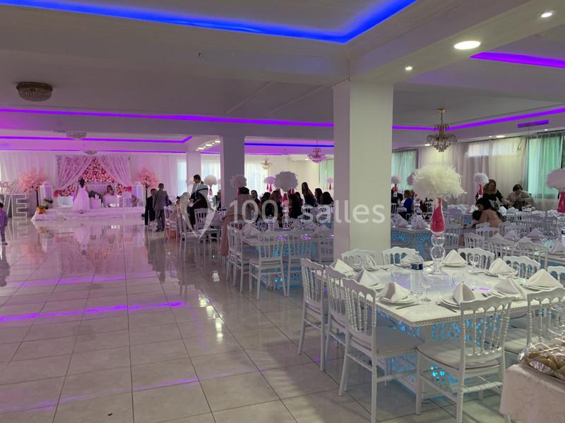 Salle de réception décorée avec des tables dressées, des invités assis et un éclairage violet.