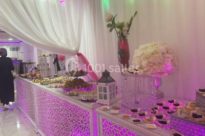 Buffet de desserts avec macarons colorés, verrines et pâtisseries disposés sur des présentoirs décoratifs dans une salle…