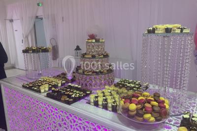 Buffet de desserts avec macarons colorés, verrines et pâtisseries disposés sur des présentoirs décoratifs dans une salle…