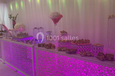 Buffet de desserts avec macarons colorés, verrines et pâtisseries disposés sur des présentoirs décoratifs dans une salle…