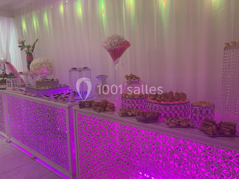 Table de buffet décorée avec des motifs lumineux roses, garnie de desserts et d'amuse-bouches variés.