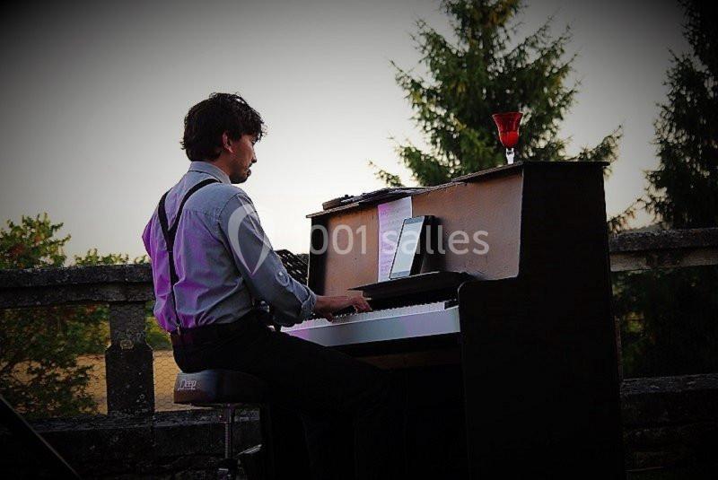 Un homme joue du piano en extérieur au coucher du soleil, avec un verre posé sur l'instrument.