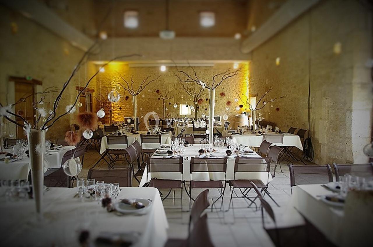 Salle de réception décorée avec des tables dressées, des branches ornées de décorations et un éclairage chaleureux.