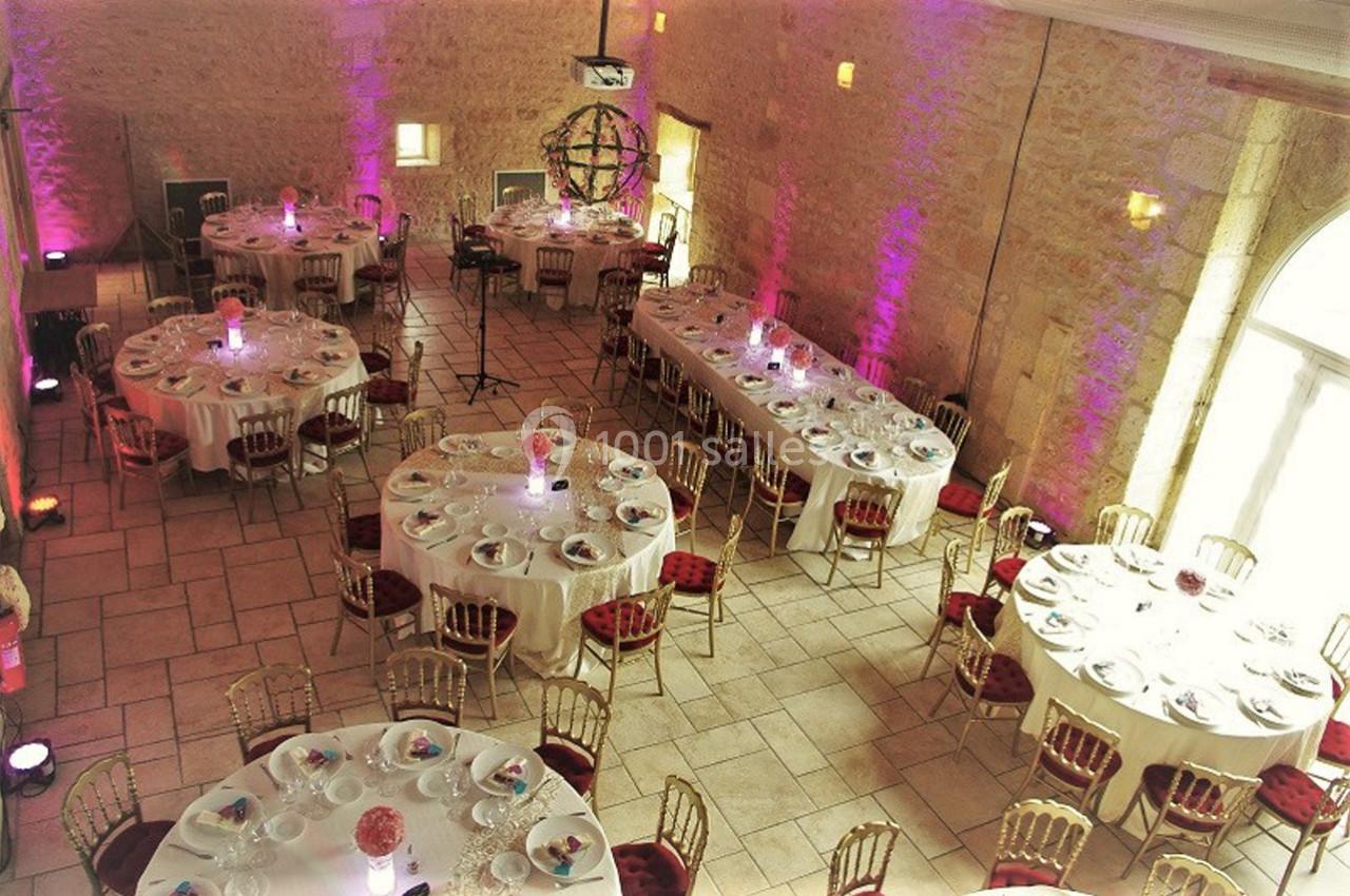 Salle de réception élégamment décorée avec des tables rondes et rectangulaires, chaises dorées et éclairage coloré.