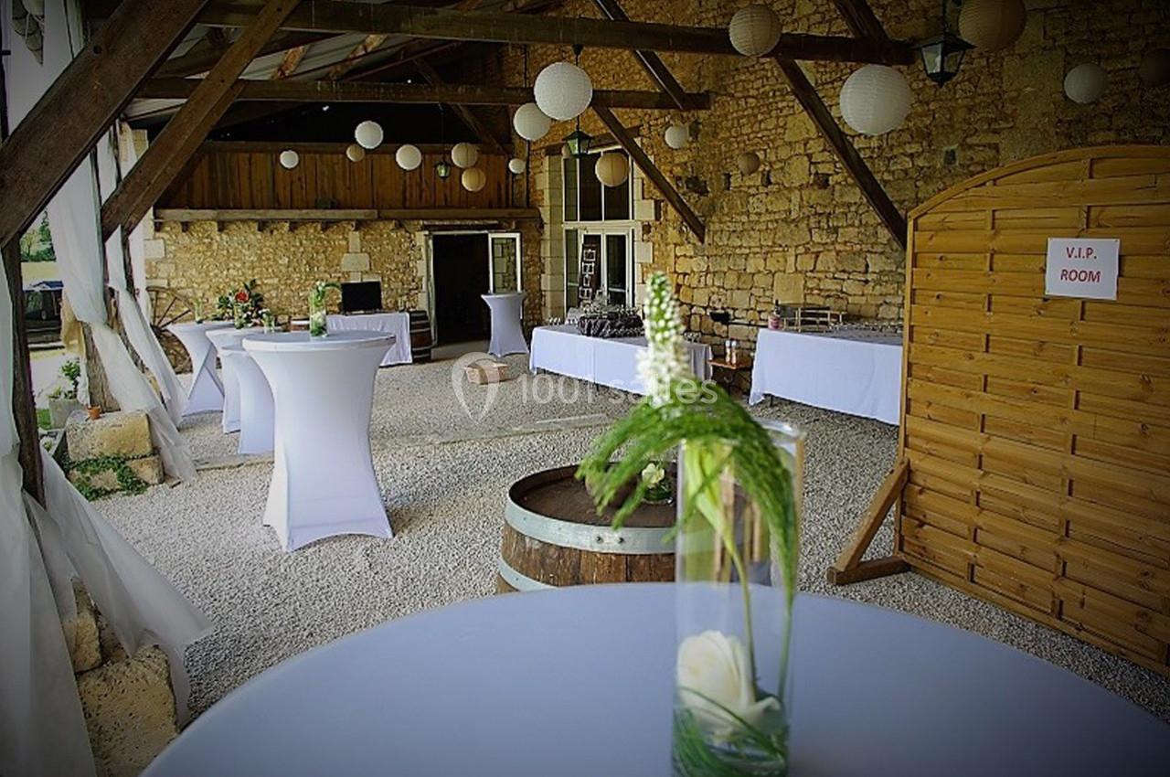Salle rustique en pierre avec tables hautes décorées, lanternes suspendues et panneau indiquant une salle VIP.