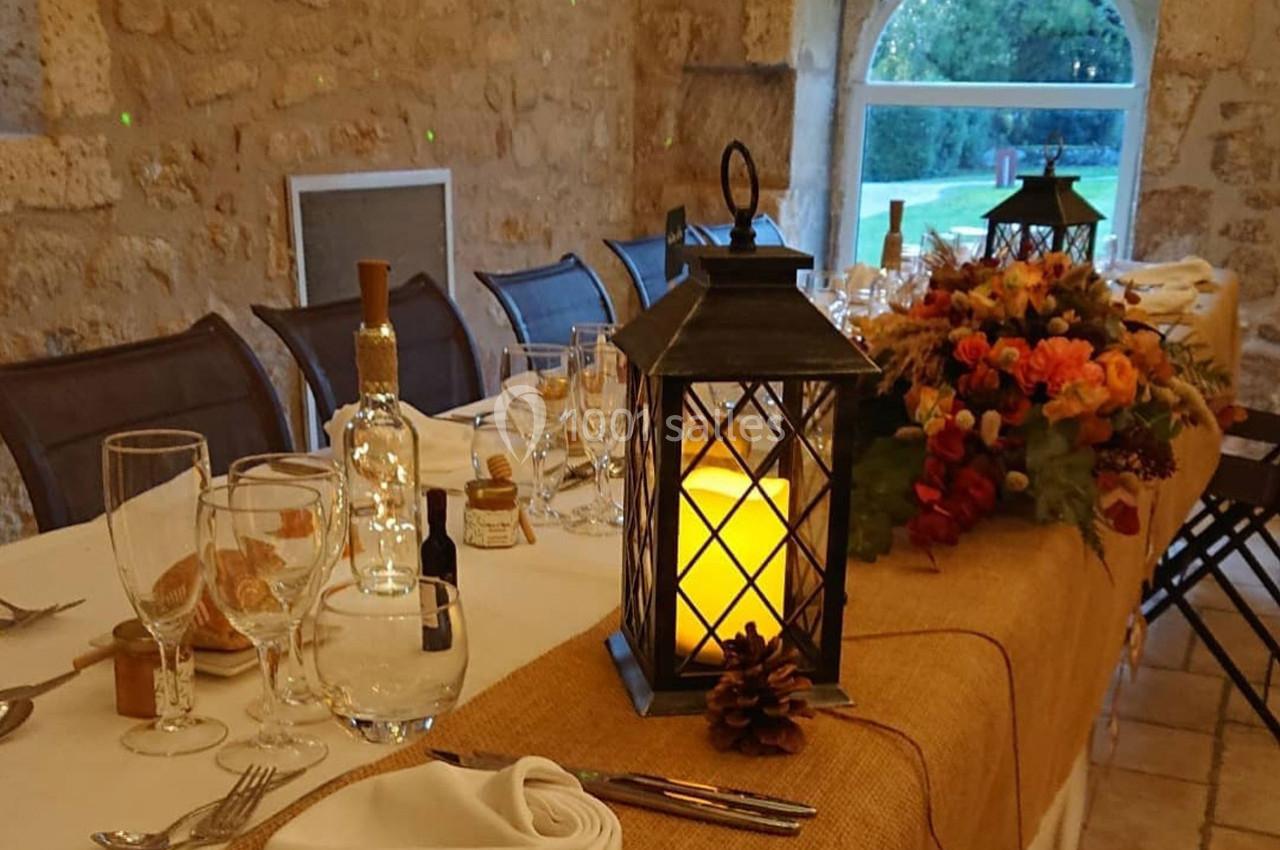 Table décorée pour un repas, avec lanterne allumée, bouquet de fleurs automnales et vaisselle élégante dans une salle en…