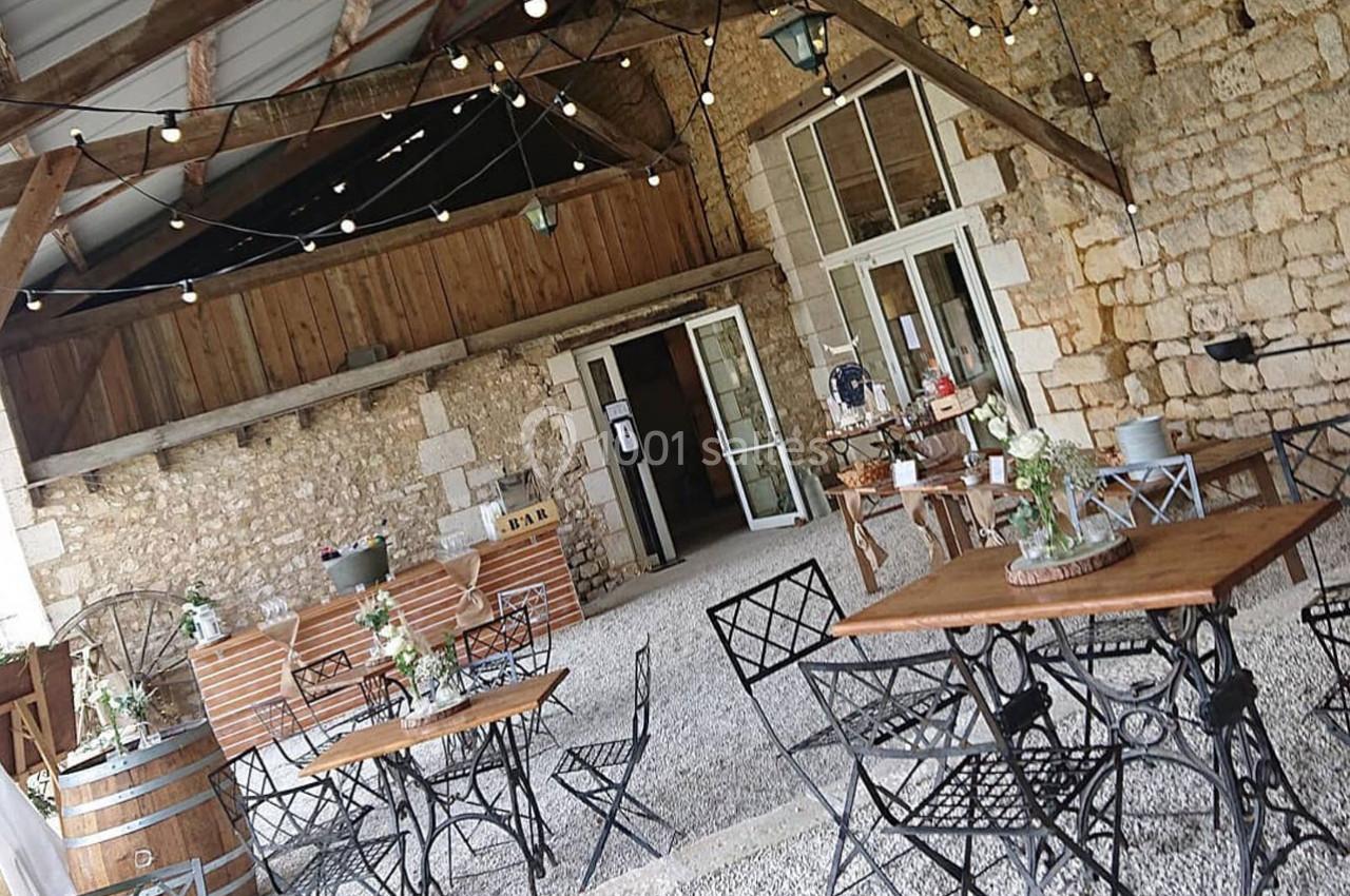 Espace extérieur couvert avec tables et chaises en métal, décoré de guirlandes lumineuses et plantes sur fond de murs en…