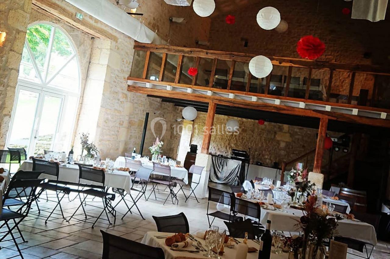 Salle de réception en pierre avec tables dressées, décorations suspendues et mezzanine en bois.