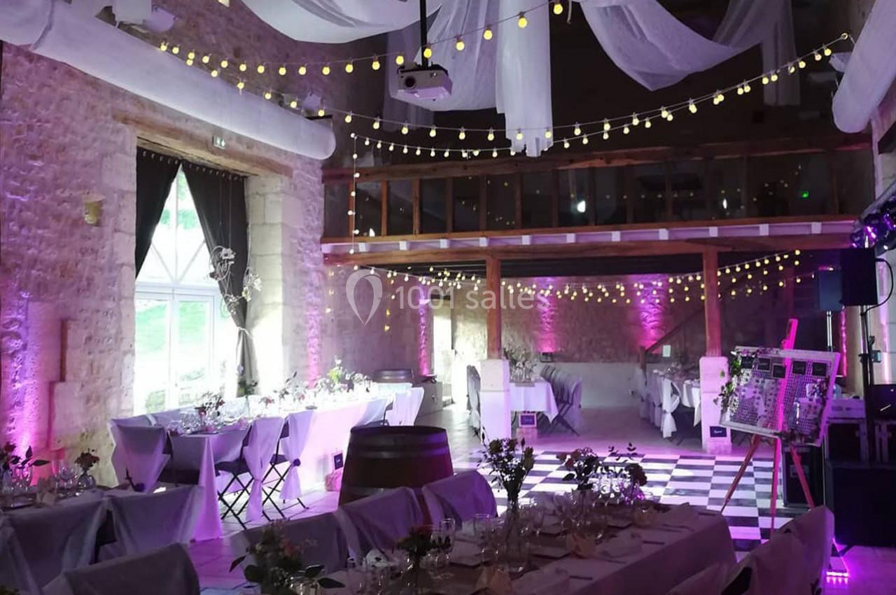 Salle de réception décorée avec des guirlandes lumineuses, des nappes blanches et une ambiance lumineuse violette.