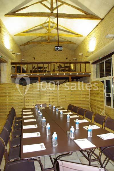 Salle de réunion avec une grande table rectangulaire, chaises, bouteilles d'eau, documents et projecteur au plafond.
