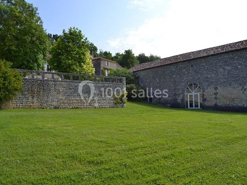 Mur en pierre et bâtiment ancien avec une grande porte vitrée, entourés d'une pelouse et d'arbres.