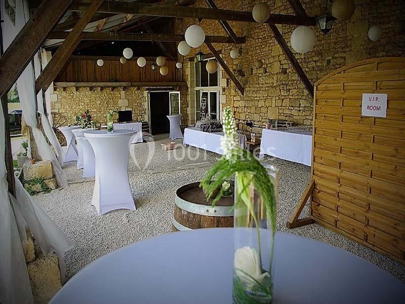 Salle de réception rustique avec murs en pierre, tables hautes décorées et lanternes suspendues.