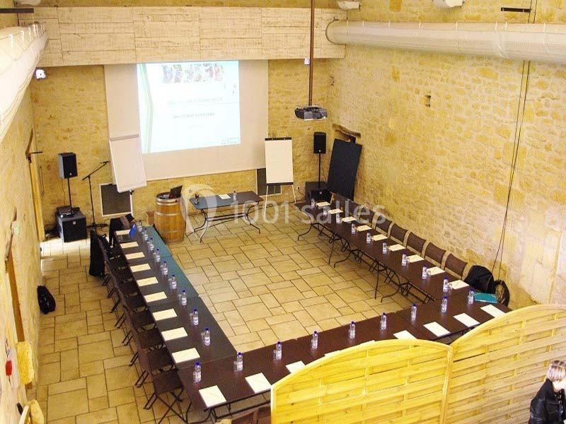 Salle de réunion en U avec tables, chaises, projecteur, écran, et murs en pierre dans un cadre lumineux.